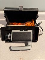 Camera resting beside open carrying case showing cloth and strap