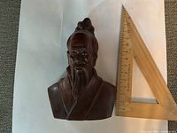 Front view of carved hardwood bust alongside ruler for scale