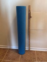 Full view of blue foam roller standing beside yardstick for scale