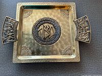 Full view of hammered brass Judaica matzah tray showing central medallion, corner grape motifs, and sculpted handles