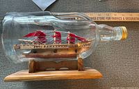 Port side view of glass bottle containing wooden ship with red sails on stand