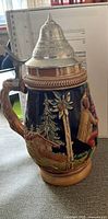 Profile view showing painted alpine scene, handle and pewter lid