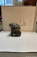 Front view of dark soapstone Inuit kneeling figure sculpture with ruler for scale