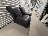 Two black leather armless couches side view in storage hallway