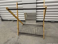 Full view of freestanding wooden and metal X-frame towel rack showing two upper bars and lower grid shelf