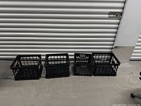Four black plastic milk-style crates aligned on floor