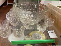 Punch bowl surrounded by several cups displayed on glass shelf