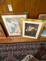 Both framed prints leaning against wood wall on rug