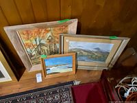 All three framed paintings leaning against wood panel wall