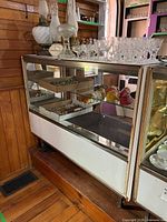 Front and side view of display case showing metal frame, glass shelves, and drawer