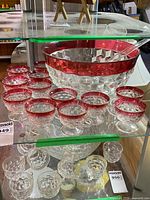 Punch bowl with surrounding ruby-rimmed cups displayed on shelf