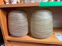 Two cylindrical beige glass shades on shelf