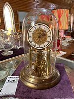 Full view of clock under glass dome on brass base