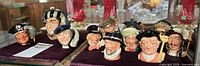 Group of 11 miniature Royal Doulton character jugs displayed in cabinet