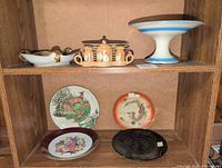 Three assorted plates on shelf include two with possible Asian themed art indicating style of lot