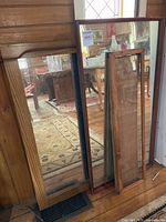 Two mirrors and an empty wooden frame leaning against wall