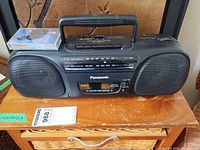 Front view of Panasonic RX-FS470 boombox with cassette tape resting on top and attached power cord