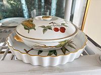 Covered casserole placed inside fluted quiche dish, showing fruit motif and gold trim