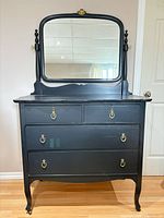 Full view of black dresser with tilt mirror, four drawers and brass hardware
