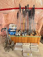 Overall lot with golf cart, clubs, shoes, balls on and in front of wooden chest