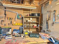 Overall view of workbench showing hand tools on pegboard, shelving with boombox, Mastercraft kit box, drill bits, extension cord and fasteners