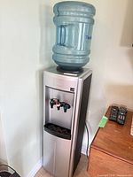 Floor standing water dispenser with jug on top, power cord visible