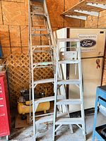 Two aluminum step ladders folded against wall