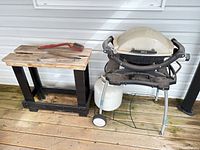 Weber grill on stand beside wooden table and brush