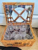 Open wicker picnic basket showing plates, cutlery and eight plastic glasses