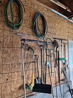 Overall view of tools hanging on wall including hoses, shovels, trimmers, rake, broom