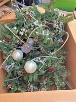 Garland in box showing ornaments, pine cones, beads, tinsel and lights