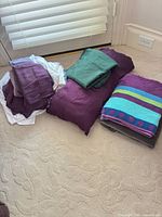 Folded purple duvet cover, white sheet, green sheet, purple pillowcases, purple throw, multicolor striped beach towel, gray bath towel