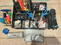 Overall view of black organizer tray, drill bits, scissors, batteries, gloves, clamps