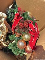 Top view of wreath and garland showing red velvet ribbon, glitter ornaments, berries and pine cones