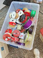Plastic bin filled with numerous ribbon spools of assorted colours and finishes
