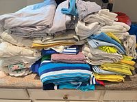 Stacked linens: sheets on top, various towels and cloths underneath