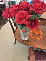 Full view of red silk flowers in cut glass vase on table