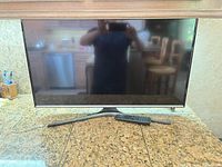 Front view of Samsung TV on stand with remote