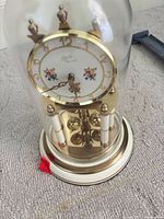 Full view of glass dome clock showing dial, base and pendulum