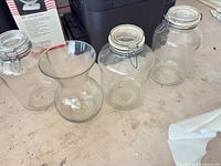 Four clear glass pieces: two swing-top storage jars, one flared vase, one cylindrical vase