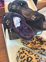 Black plush slippers on shoebox with leopard pair beneath