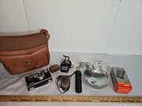 Lot overview showing camera, bag, light meter, flash, reflector, film canisters, filter tin, boxed accessory