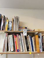 Two shelves showing upright cookbooks, stack of magazines, puzzle digests