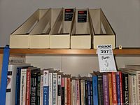 Upper shelf showing books and five beige magazine holders