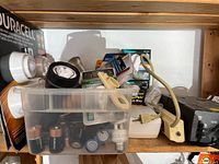 Overall lot on shelf showing packaged Duracell puck lights, batteries, bulbs, extension cord and UPS