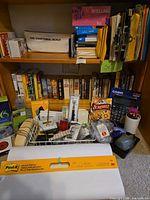 Overall view of bookshelf with books, office supplies, electronics boxes, Scrabble game