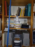 Shelf stereo, speakers, portable CD player, stacks of cassettes, CDs and books in shelving unit