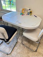 Overall view of white laminate table with two chrome vinyl chairs