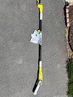 Full view of Ryobi corded telescoping pole saw with accessories on pavement