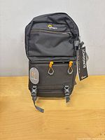 Front view of Lowepro Slingshot SL 250 AW III showing orange zipper pulls, buckles, attached tags